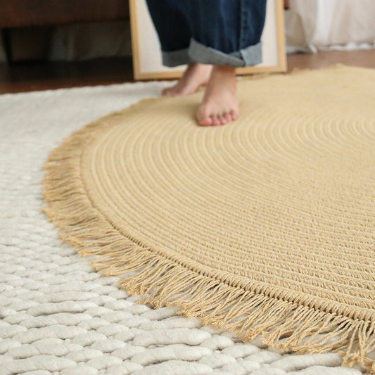 Round beige rug with fringes on a light gray rug, person wearing jeans partially visible.